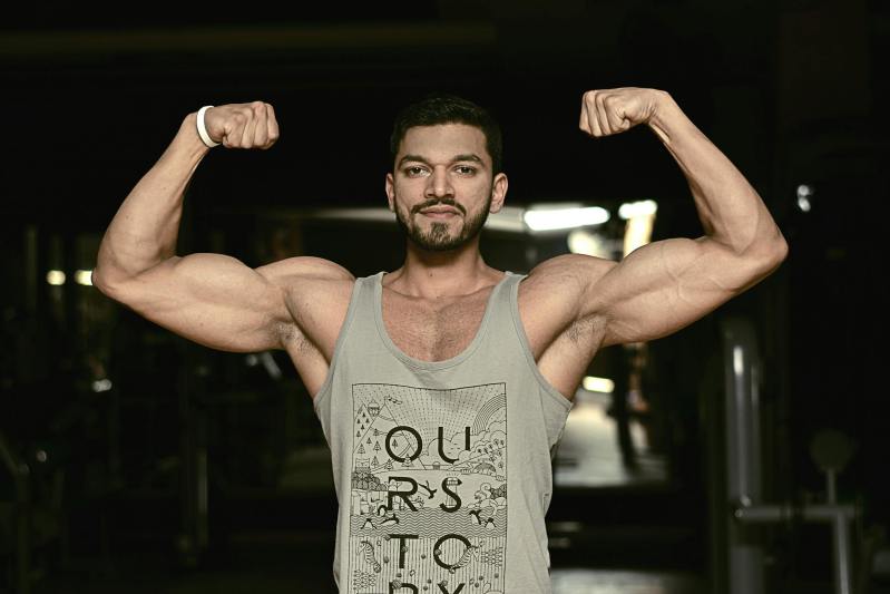 Man flexing arms muscles on a dark background in the gym